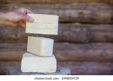 Fuel Briquettes Lie On A Wooden Hemp. A Man's Hand Holds A Fuel Briquette.