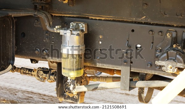 A fuel filter in a truck. A dirty clear\
fuel filter with black rubber hose mounted on a vehicle chassis\
with copy space with copy space. Selective\
focus