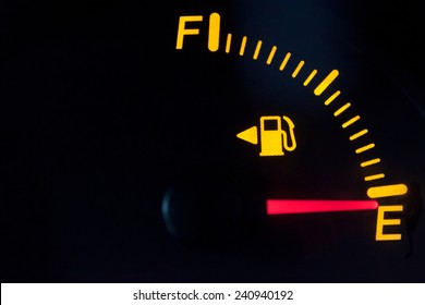 Fuel gauge showing empty tank. Yellow glowing and lit meter with red needle. Isolated against a black background. - Powered by Shutterstock