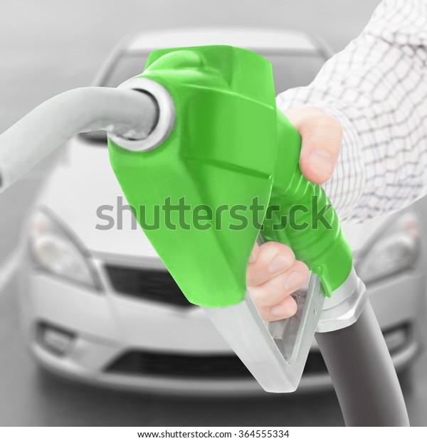 Fuel pump gun in hand with car on background -\
studio shot