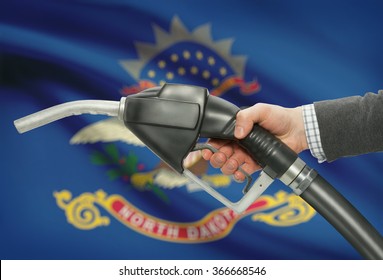 Fuel pump nozzle in hand with US states flags on background - North Dakota
