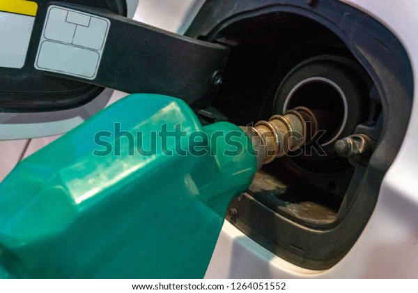 Fuelling gun\
inserted into the tank of white\
car.