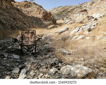 Fujairah, United Arab Emirates - April 14, 2022: Camouflage folding camping chair in rugged, rocky terrain in a desert wadi (ravine). Wild desert adventure camping concept.