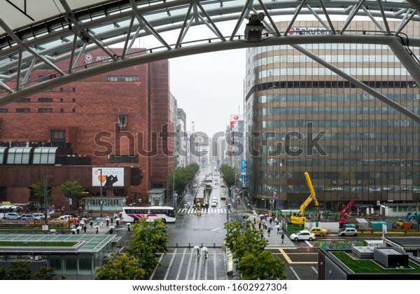 Fukuoka,\
Japan - Oct 6 2017: Cityscape of huge financial buildings in Hakata\
Station business district. Main road under construction. Busy\
passengers with umbrella in cloudy rainy\
day.