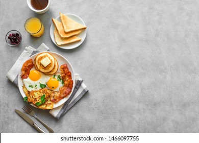 Full American Breakfast on gray, top view, copy space. Sunny side fried eggs, roasted bacon, hash brown, pancakes, toasts, orange juice and coffee for breakfast. - Shutterstock ID 1466097755