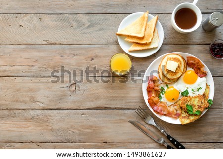 Full American Breakfast on wooden, top view, copy space. Sunny side fried eggs, roasted bacon, hash brown, pancakes, orange juice and coffee for breakfast.