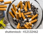 Full ashtray with smoked cigarettes and lot of ashes on white table. Lighter and the cigarettes near it