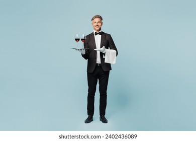 Full body adult barista sommelier male waiter butler man wear shirt black suit bow tie uniform hold tray two glasses of wine work at cafe isolated on plain blue background. Restaurant employee concept - Powered by Shutterstock