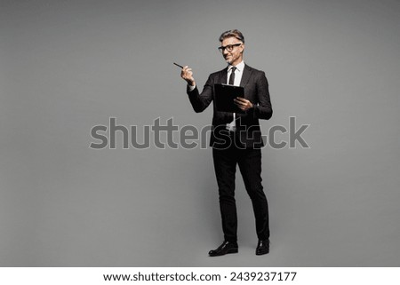 Full body adult employee business man corporate lawyer he wearing black suit shirt tie work in office hold clipboard with paper account documents point finger aside isolated on plain grey background