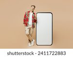 Full body adult man wear red shirt white t-shirt casual clothes point thumb finger on big huge blank screen mobile cell phone smartphone with area isolated on plain pastel light beige color background
