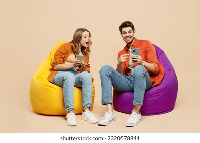 Full body amazed young couple two friends family man woman wear casual clothes together sit in bag chair hold in hand use mobile cell phone isolated on pastel plain light beige color background studio - Powered by Shutterstock