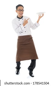 Full Body Asian Chef Holding And Pointing To An Empty Plate, Standing Isolated On White Background.