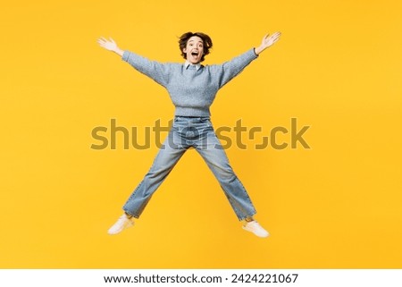 Full body astonished fun young woman she wears grey knitted sweater shirt casual clothes jump high with outstretched hands arms isolated on plain yellow background studio portrait. Lifestyle concept