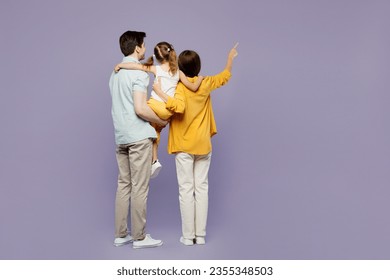 Full body back rear view young parents mom dad child kid girl 6 years old wearing blue yellow casual clothes hold daughter point finger aside isolated on plain purple background. Family day concept