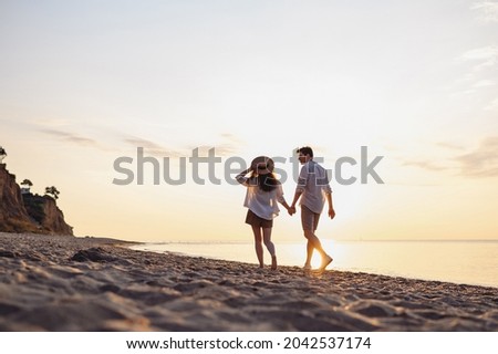 Full body back rear view young couple two friends family man woman in white shirt clothes hold hands walk stroll together at sunrise over sea beach ocean outdoor exotic seaside in summer day evening