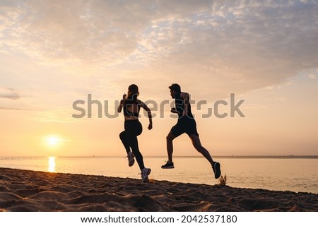 Full body back view couple young friends sporty sportsman sportswoman woman man in sport clothes warm up training running jog on seaside sunrise over sea sand ocean beach outdoor in summer day morning