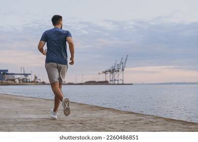 Full body back view young strong sporty athletic toned fit sportsman man in sports clothes warm up training run jog at sunrise sun over sea beach outdoor on pier seaside in summer day cloudy morning. - Powered by Shutterstock