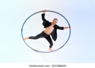Full body barefoot man in jeans   black shirt doing trick cyr wheel during performance against gradient blue background
