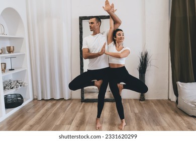 Full body of barefoot multiethnic couple in black and white sportswear standing on floor in tree pose during yoga session at home - Powered by Shutterstock