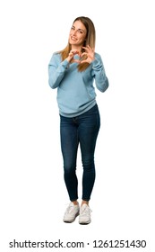 Full Body Of Blonde Woman With Blue Shirt Making Heart Symbol By Hands On White Background