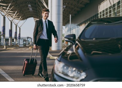 Full body bottom view young traveler businessman young man in black dinner suit going walk outside at international airport terminal with suitcase to car booking taxi Air flight business trip concept.