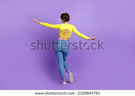 Full body cadre of relaxed flying slim woman bob hair wearing stylish crop top open spine with jeans isolated on purple color background