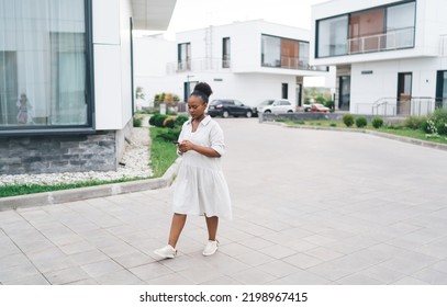 Full Body Of Casual African American Lady In Light White Dress Browsing Mobile Phone While Walking On Paved Road In Modern City Neighborhood