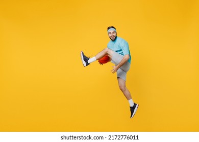 Full Body Caucasian Young Fitness Trainer Instructor Sporty Man Sportsman In Headband Blue T-shirt Hold Ball Play Basketball Game Jump High Isolated On Plain Yellow Background. Workout Sport Concept