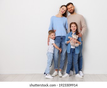 Full Body Of Cheerful Family With Little Kids Looking At Camera While Standing Together On Floor Near Wall In Empty Room Of New Home