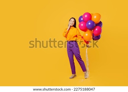 Full body cheerful side profile view happy fun young woman wearing casual clothes celebrating holding face bunch of balloons isolated on plain yellow background. Birthday 8 14 holiday party concept