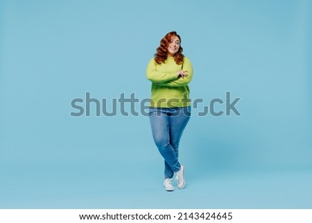 Full body confident happy young chubby overweight plus size big fat fit woman wear green sweater hold hands crossed folded isolated on plain blue background studio portrait. People lifestyle concept