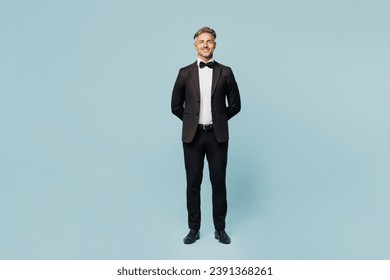 Full body confident smiling fun adult barista male waiter butler man wear shirt black suit bow tie uniform looking camera work at cafe isolated on plain blue background. Restaurant employee concept