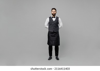 Full body confident young barista male waiter butler man 20s wear white shirt vest elegant uniform work at cafe looking camera isolated on plain grey background studio. Restaurant employee concept.