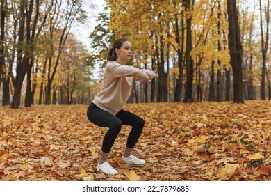 Full Body Of Confident Young Female Athlete In Activewear Squatting In Autumn Park While Having Fitness Training In Nature 