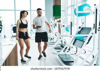 Full Body Of Content Instructor With Sporty Woman In Activewear Walking In Fitness Club While Choosing Gym Equipment For Workout