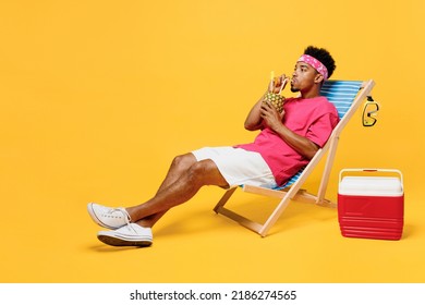 Full Body Cool Fun Happy Young Man 20s He Wear Pink T-shirt Bandana Lying On Deckchair Sunbad Near Hotel Pool Drink Pineapple Juice Isolated On Plain Yellow Background Summer Vacation Sea Rest Concept
