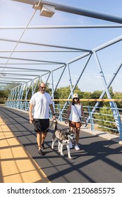 Full Body Of Couple With Cute Husky Dog On Leash Strolling Together On Empty Footbridge On Summer Day In City