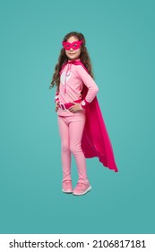 Full Body Of Cute Child Wearing Pink Superhero Cloak And Mask Standing With Hands On Waist And Looking At Camera On Blue Background