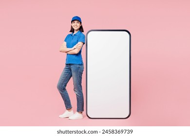 Full body delivery employee woman wears blue cap t-shirt uniform workwear work as dealer courier stand near big huge blank screen mobile cell phone with empty area isolated on plain pink background - Powered by Shutterstock