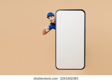 Full body delivery guy employee man wear blue cap t-shirt uniform workwear work as dealer courier stand behind point on big huge blank screen area mobile cell phone isolated on plain beige background - Powered by Shutterstock