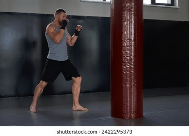 Full body of determined male athlete in sportswear in front of red punching bag. Sportsman with his hands wrapped in boxing tapes in gym during training. - Powered by Shutterstock