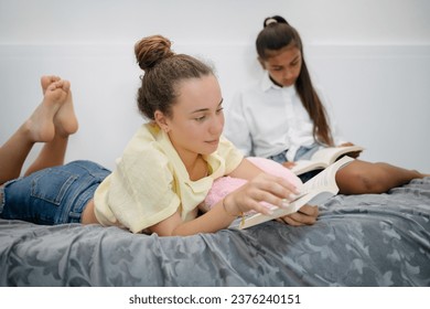 Full body of diverse teen girlfriends lying on bed and reading books together - Powered by Shutterstock