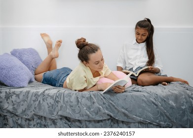 Full body of diverse teen girlfriends lying on bed and reading books together - Powered by Shutterstock