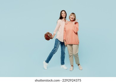 Full body elder parent mom with young adult daughter two women together wear casual clothes hold in hand bouquet of flowers look camera hug isolated on plain blue cyan background. Family day concept - Powered by Shutterstock