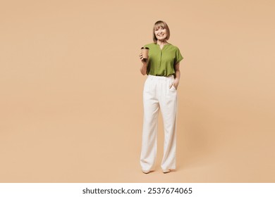 Full body elderly blonde woman 50s years old she wear green shirt casual clothes hold takeaway delivery craft paper brown cup coffee to go isolated on plain pastel beige background. Lifestyle concept - Powered by Shutterstock