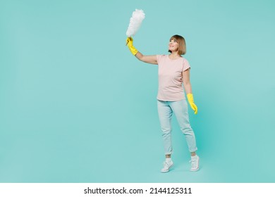 Full body elderly housewife woman 50s in pink t-shirt gloves doing housework hold white duster brush isolated on plain pastel light blue background studio. Housekeeping cleaning tidying up concept.