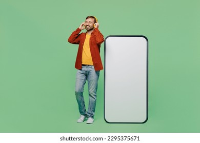 Full body elderly man 40s years old wears casual clothes red shirt t-shirt headphones big huge blank screen mobile cell phone with area listen to music isolated on plain pastel light green background - Powered by Shutterstock