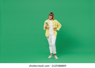 Full body elderly smiling fun happy woman 50s in glasses yellow shirt using hold in hand mobile cell phone browse internet isolated on plain green background studio portrait People lifestyle concept - Powered by Shutterstock