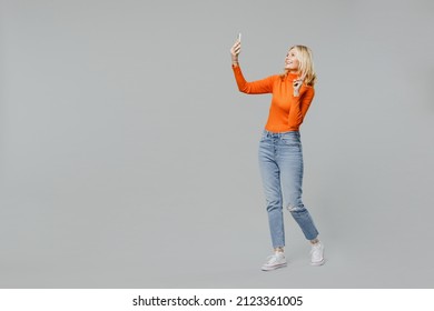 Full body elderly smiling happy blonde woman 50s in orange turtleneck doing selfie shot on mobile cell phone post photo on social network show v-sign isolated on plain grey background studio portrait. - Powered by Shutterstock