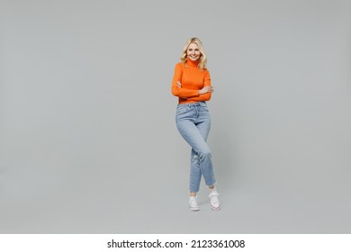 Full Body Elderly Smiling Happy Blonde Caucasian Woman 50s In Orange Turtleneck Hold Hands Crossed Folded Look Camera Isolated On Plain Grey Color Background Studio Portrait. People Lifestyle Concept